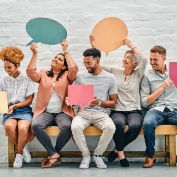 A group of diverse young people holding up colorful signs that look like talk boxes, symbolizing the importance of finding and using your unique voice in blogging.