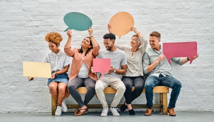 A group of diverse young people holding up colorful signs that look like talk boxes, symbolizing the importance of finding and using your unique voice in blogging.