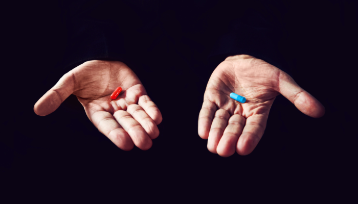 Holding a red and blue pill in each hand
